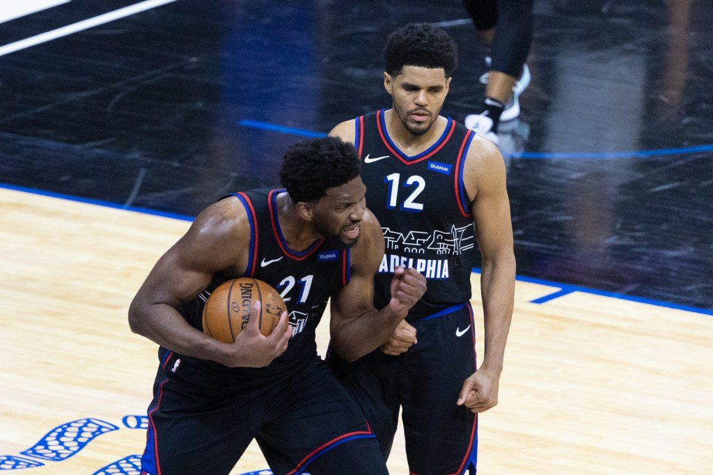 Sixers center Joel Embiid celebrates with the ball in his hand as Tobias Harris joins him